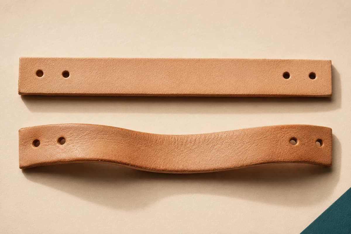 Two leather sandal straps side by side, the upper one stiff and straight, the lower one softened and curved after wear